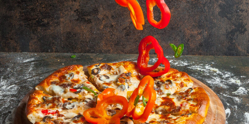 Side view pizza with slices of bell pepper and pizza slices and flour in board cookware on stone background