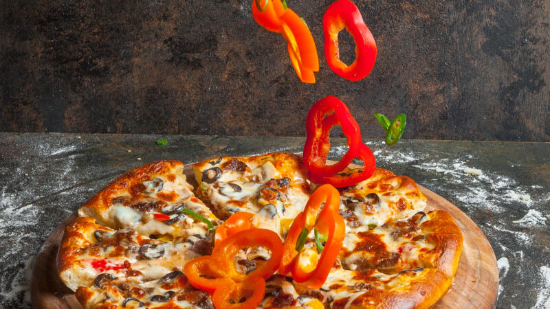 Side view pizza with slices of bell pepper and pizza slices and flour in board cookware on stone background